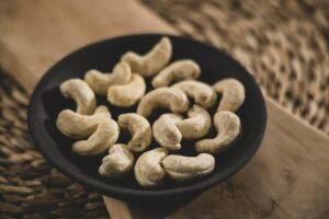 A close-up image of cashew nuts in a black bowl on a wooden surface, showcasing their natural texture.